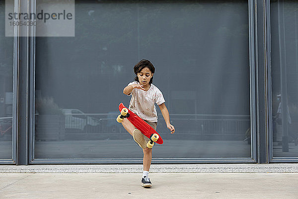 Junge übt Stunt mit dem Skateboard  während er auf dem Gehweg gegen die Wand steht