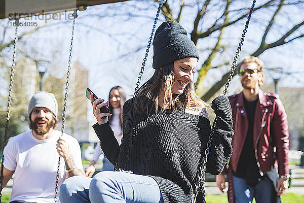 Glückliche junge Frau beim Schwingen mit Freunden im Park