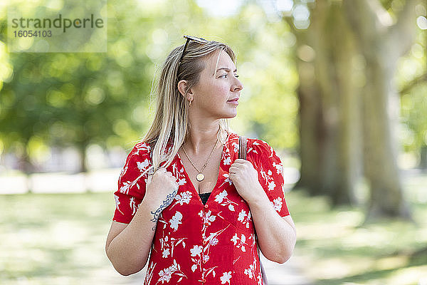 Nachdenkliche Frau steht in einem öffentlichen Park an einem sonnigen Tag