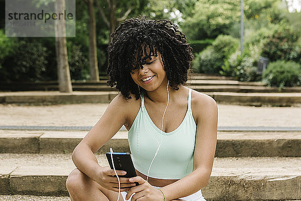 Sportliche junge Frau benutzt Smartphone im Park