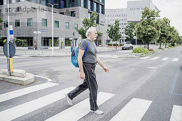 Älterer Mann mit Rucksack überquert Straße in der Stadt