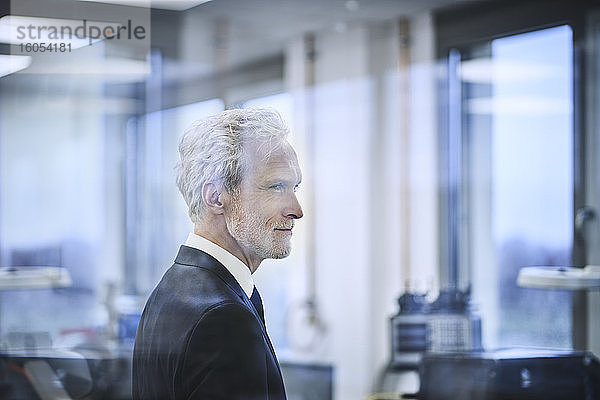 Nachdenklicher männlicher Manager hinter Glas in einer Fabrik