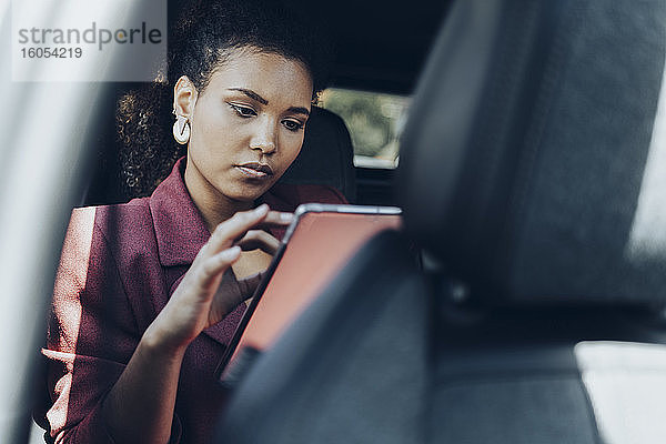 Junge Geschäftsfrau  die im Auto sitzend ein digitales Tablet benutzt