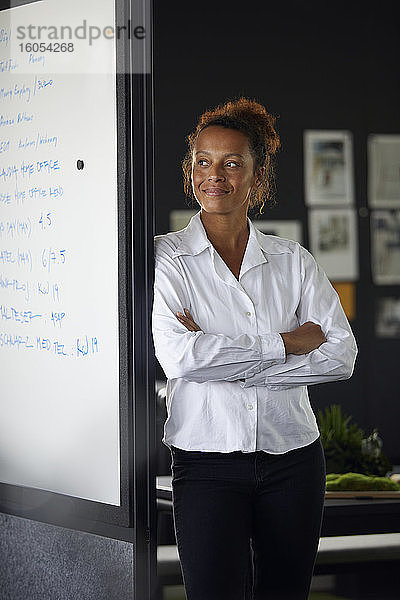 Porträt einer lächelnden Geschäftsfrau  die sich in einem modernen Büro an ein Flipchart lehnt