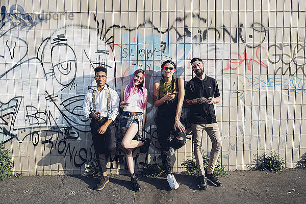 Porträt einer lächelnden Gruppe von Freunden  die an einer Graffiti-Wand in der Stadt stehen