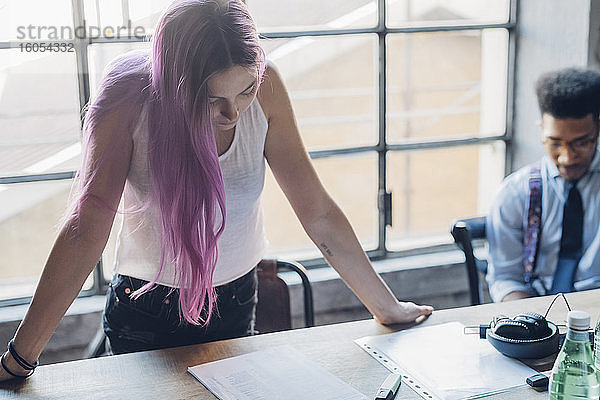 Junge Frau mit rosa Haaren lehnt sich an einen Tisch in einem Loft-Büro