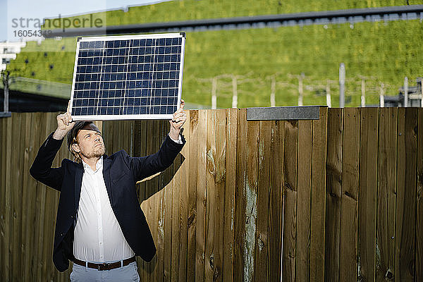 Geschäftsmann steht an einer Tafel und hält ein Solarpanel hoch