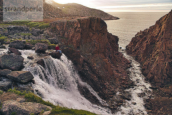 Junge Frau sitzt auf einem Felsen am Wasserfall  Teriberka  Murmansk Oblast  Russland
