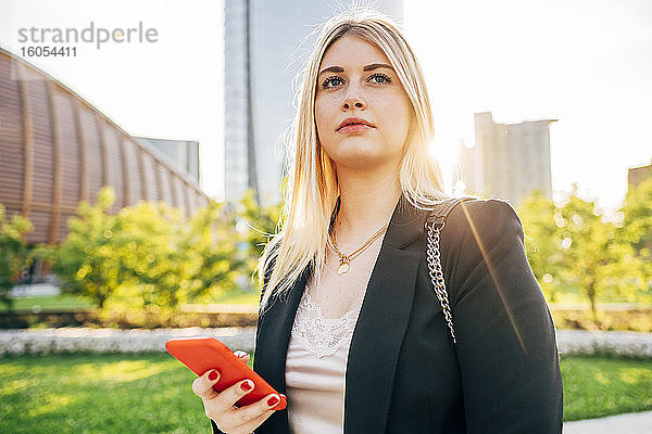 Nahaufnahme einer nachdenklichen Geschäftsfrau  die ein Smartphone hält  während sie in der Stadt steht