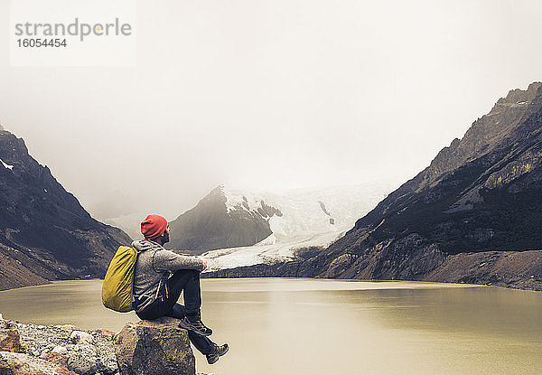 Mann mit Rucksack sitzt auf einem Felsen am See in Patagonien  Argentinien