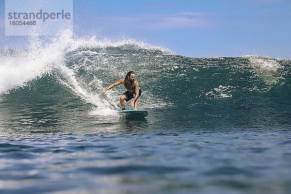 Männlicher Surfer ohne Hemd  der auf dem Meer gegen den Himmel surft  Bali  Indonesien