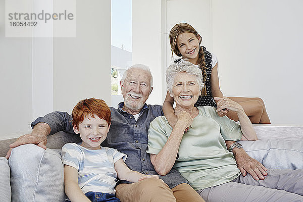Porträt von glücklichen Großeltern mit Enkelkindern auf einer Couch in einer Villa