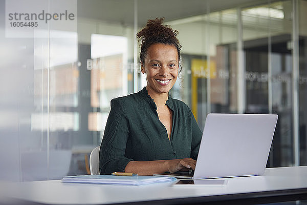 Porträt einer lächelnden Geschäftsfrau  die an einem Laptop am Schreibtisch arbeitet