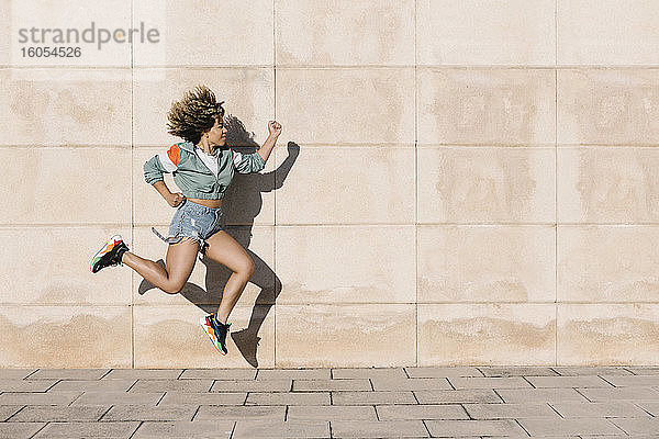 Junge Frau springt an einem sonnigen Tag gegen die Wand