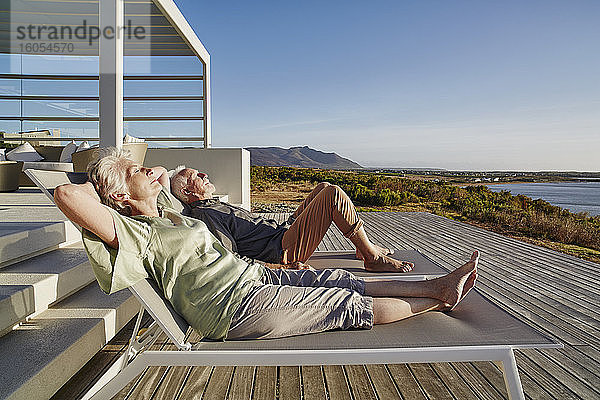 Älteres Paar liegt auf Liegestühlen in einem luxuriösen Strandhaus
