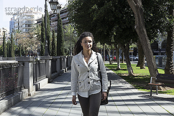 Stilvolle Geschäftsfrau schaut weg  während sie auf dem Fußweg im Park spazieren geht