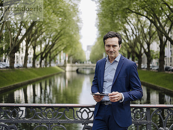 Porträt eines selbstbewussten reifen Geschäftsmannes auf einer Brücke stehend mit Tablet
