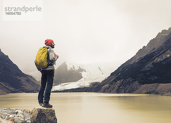 Älterer Mann mit Rucksack steht auf einem Felsen am See in Patagonien  Argentinien
