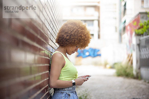 Frau mit Afro-Haar  die ein Smartphone benutzt  während sie an einer Mauer steht