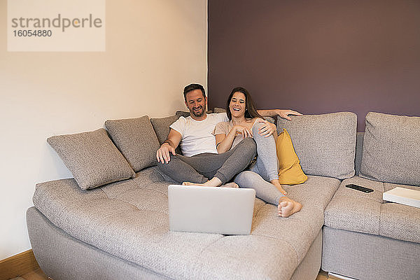Glückliches Paar  das sich auf dem Sofa zu Hause auf dem Laptop einen Film ansieht