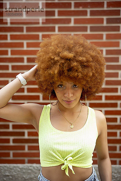 Nahaufnahme einer Frau mit braunem Afro-Haar  die an einer Backsteinmauer steht