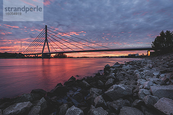 Deutschland  Nordrhein-Westfalen  Wesel  Felsiges Rheinufer bei dramatischem Sonnenuntergang mit Niederrheinbrücke Wesel im Hintergrund