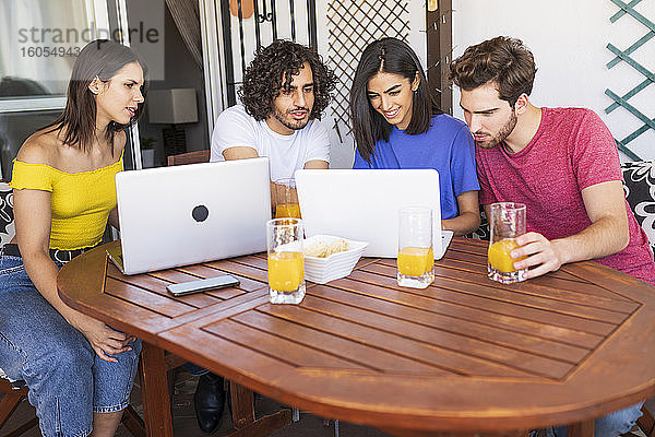 Junge Männer und Frauen teilen sich einen Laptop  während sie am Tisch im Hinterhof sitzen