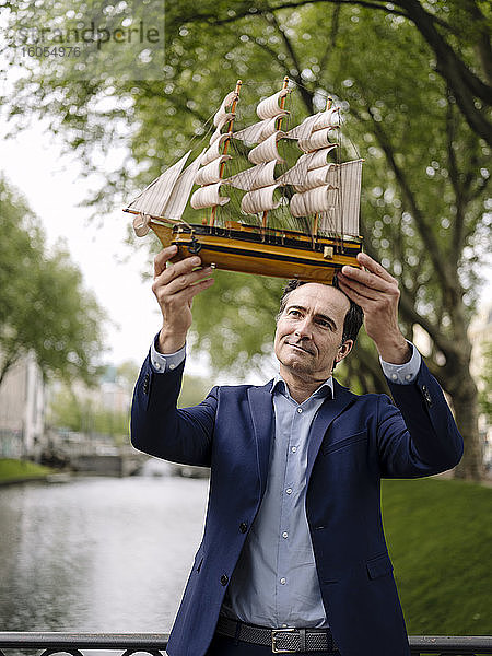 Älterer Geschäftsmann hält Modell-Segelschiff auf einer Brücke