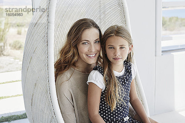 Porträt einer lächelnden Mutter und ihrer Tochter  die in einem Hängesessel sitzen