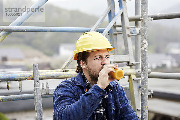 Arbeiter trinkt Saft auf einem Baugerüst auf einer Baustelle