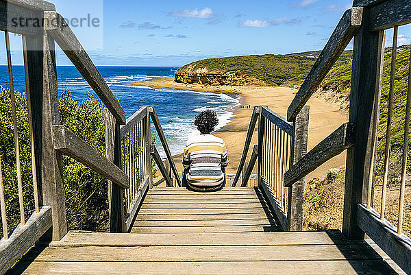 Mann schaut auf Bells Beach  während er auf einer Holztreppe sitzt  Victoria  Australien