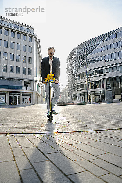 Geschäftsmann mit Kick-Scooter und Blumenstrauß in der Stadt