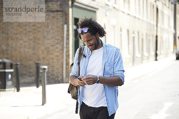 Junger Mann mit Rucksack steht auf der Straße und schaut auf sein Handy  London  UK