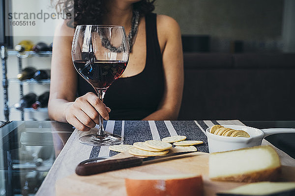 Junge Frau hält ein Weinglas  während sie am Esstisch sitzt