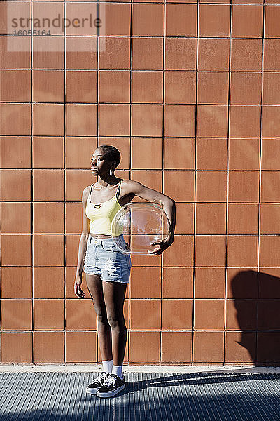 Nachdenkliche junge Frau  die einen Glasbehälter hält  während sie auf dem Gehweg in der Stadt steht