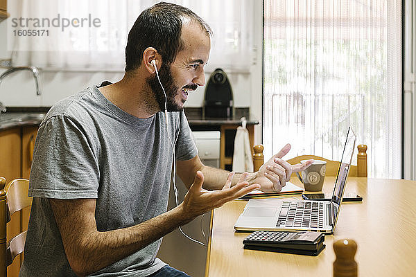 Mittelgroßer erwachsener Mann  der bei der Arbeit zu Hause Videokonferenzen auf seinem Laptop abhält