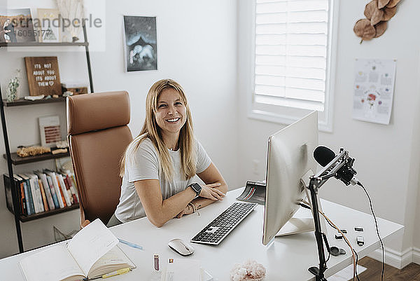 Lächelnde Geschäftsfrau  die zu Hause einen Computer auf dem Schreibtisch benutzt