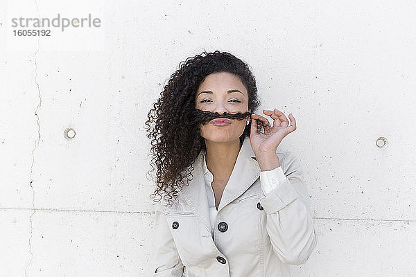 Stilvolle Geschäftsfrau hält Haare auf den Lippen wie Schnurrbart gegen die Wand