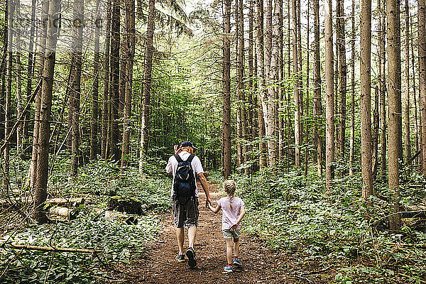 Mann hält die Hände seiner Tochter beim Wandern im Wald