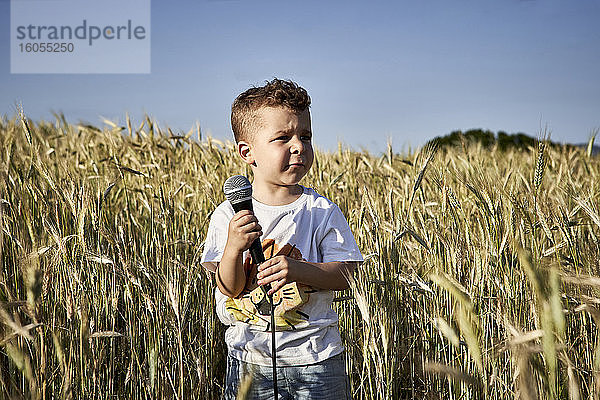 Junge  der ein Mikrofon hält und wegschaut  während er inmitten von Feldfrüchten vor einem klaren Himmel steht