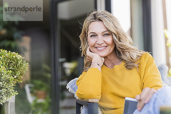 Porträt einer glücklichen reifen Frau  die mit einem digitalen Tablet auf einer Terrasse sitzt