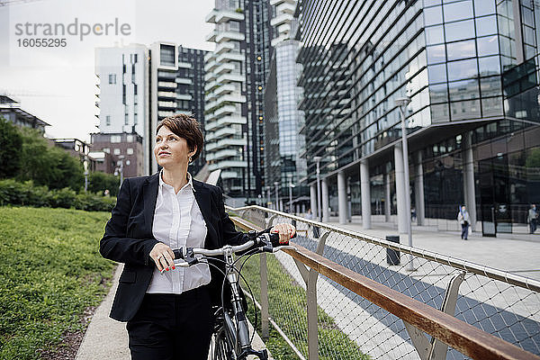 Weibliche Fachkraft mit Fahrrad schaut weg  während sie gegen Gebäude in der Stadt läuft