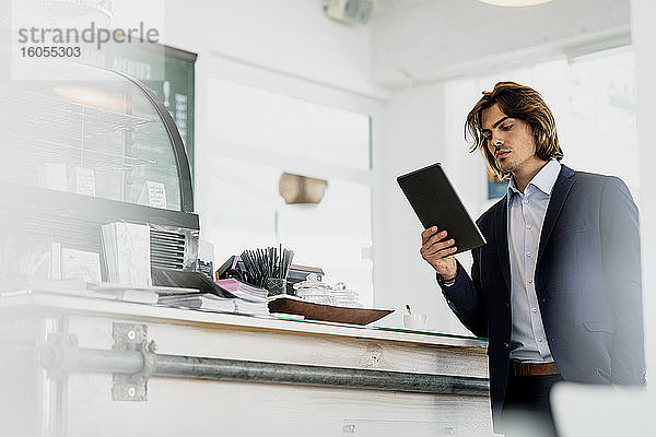 Männlicher Unternehmer  der ein digitales Tablet benutzt  während er in einem Kaffeehaus steht