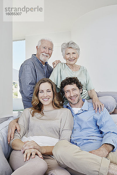 Porträt eines glücklichen älteren Paares mit erwachsenen Kindern  die auf einer Couch in einer Villa sitzen