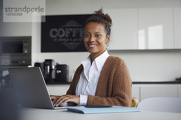 Porträt einer lächelnden Geschäftsfrau  die in der Küche am Laptop arbeitet