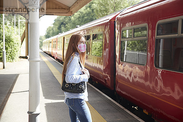 Junge Frau mit Gesichtsschutz auf dem Bahnsteig eines Bahnhofs