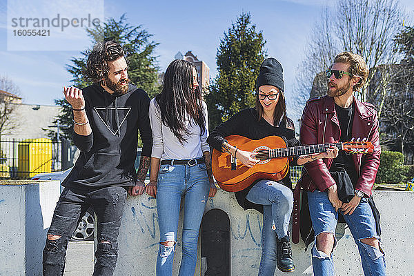 Mittlere erwachsene Frau spielt Gitarre  während sie sich mit Freunden in der Stadt vergnügt