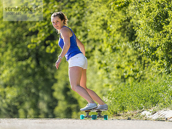 Junge Frau Skateboarding auf der Straße von Pflanzen während sonnigen Tag
