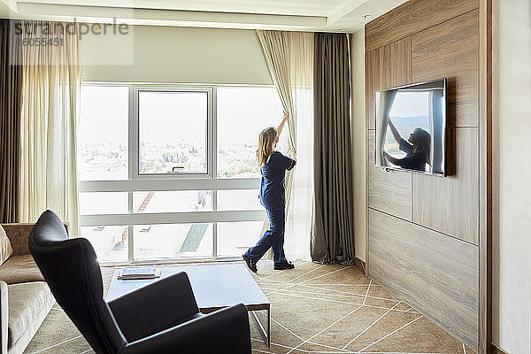 Zimmermädchen öffnet die Vorhänge eines Fensters im Hotelzimmer