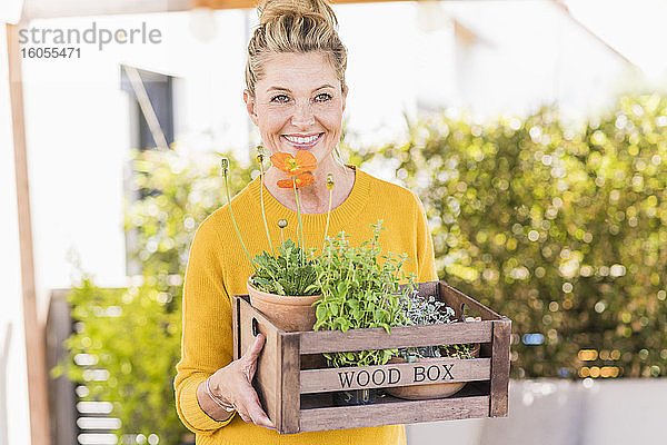 Porträt einer glücklichen reifen Frau mit Holzkiste mit Pflanzen auf der Terrasse